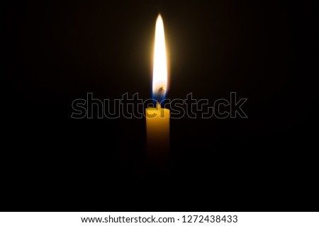 A single candle light glowing on a yellow candle in the middle part of frame on black background, a single candle light glowing in a dark room