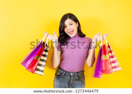 Portrait photograph of the beautiful Asian girl age between 20 - 30 years old enjoying shopping and a lot of shopping bags in her hand close up with yellow background.