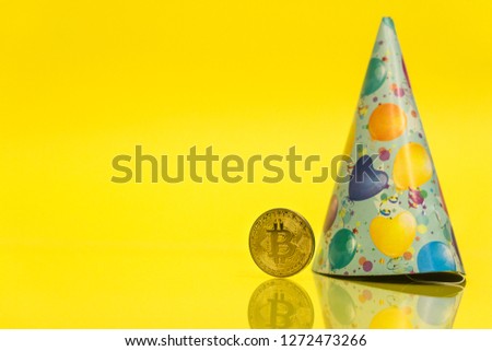 Bitcoin cryptocurrency celebrating birthday - 10 years, coin with birthday hat behind it, with yellow copy space