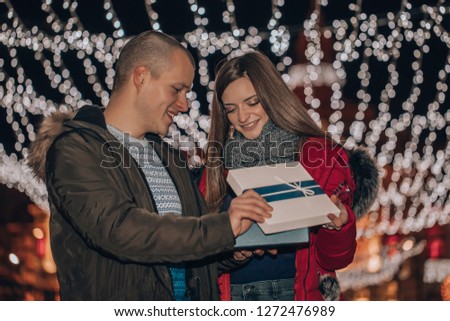 Young couple together opens box with a gift. The woman gives a man present winter evening. Romantic people with love. - Image