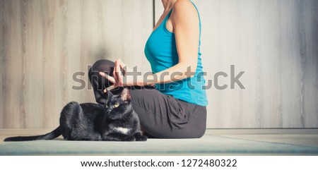 woman doing yoga at home - black cat sitting next to her