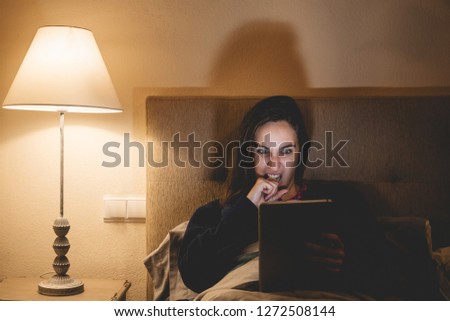 Woman in pajamas politics fight in bed stirring on tablet or cell phone impregnated at what she sees before sleeping. Girl on the touch screen about to sleep disturbing the scared sleep
