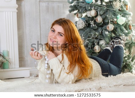 Beautiful girl in the New Year's studio. She sits by the Christmas tree with lights.
