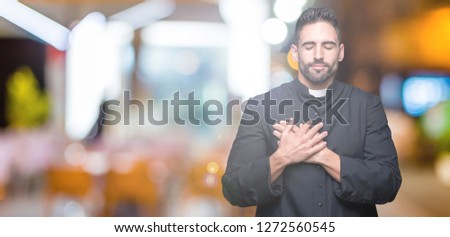 Young Christian priest over isolated background smiling with hands on chest with closed eyes and grateful gesture on face. Health concept.