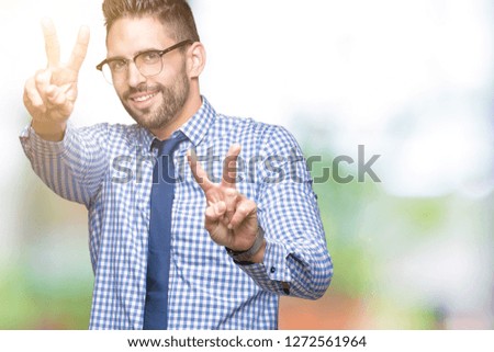 Young business man wearing glasses over isolated background smiling looking to the camera showing fingers doing victory sign. Number two.