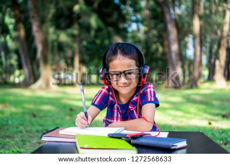 Little girl listening to music while studying at park