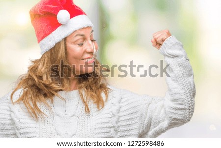 Middle age senior hispanic woman wearing christmas hat over isolated background showing arms muscles smiling proud. Fitness concept.