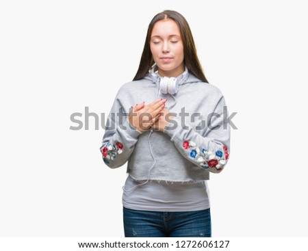 Young beautiful caucasian student woman wearing headphones over isolated background smiling with hands on chest with closed eyes and grateful gesture on face. Health concept.