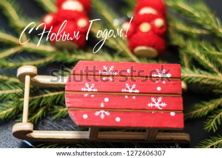 Christmas card. Bright red Santa's sleigh with snowflakes on the background of a Christmas tree and a wooden baby in bright red knitted clothes. The inscription happy NEW YEAR in Russian !
