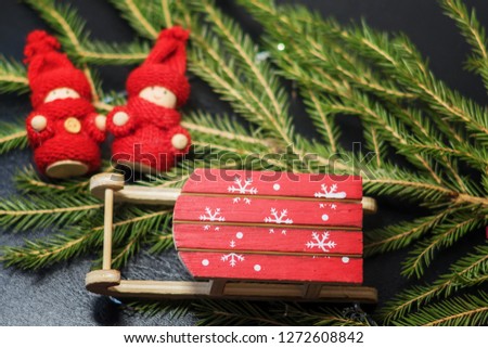 Christmas card. Bright red Santa's sleigh with snowflakes on the background of a Christmas tree and a wooden baby in bright red knitted clothes.