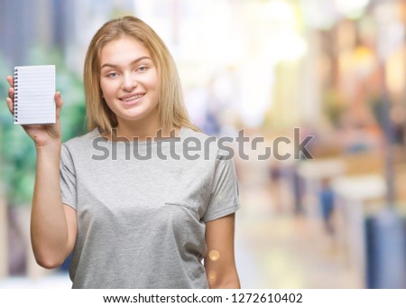 Young caucasian woman holding blank notebook over isolated background with a happy face standing and smiling with a confident smile showing teeth