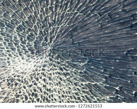  Hole and cracks in the glass of window. Cracked glass texture against the sky. Cracked glass with a hole from a bullet with spiral web pattern

