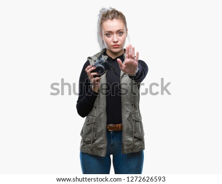 Young blonde woman taking pictures using vintage camera over isolated background with open hand doing stop sign with serious and confident expression, defense gesture