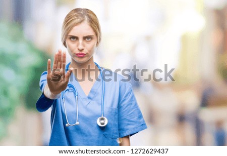 Young beautiful blonde doctor surgeon nurse woman over isolated background doing stop sing with palm of the hand. Warning expression with negative and serious gesture on the face.