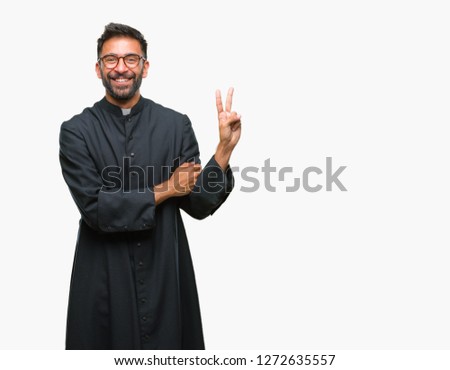 Adult hispanic catholic priest man over isolated background smiling with happy face winking at the camera doing victory sign. Number two.