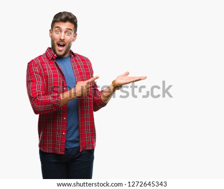 Young handsome man over isolated background amazed and smiling to the camera while presenting with hand and pointing with finger.