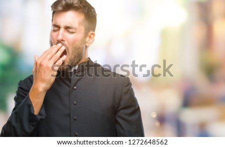 Young catholic christian priest man over isolated background bored yawning tired covering mouth with hand. Restless and sleepiness.