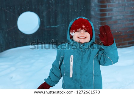 happy little boy playing in winter. child in gloves waving his hand and smiling