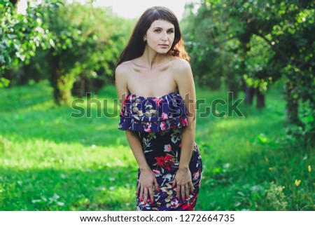 Young beautiful brunette girl in a blue dress in the summer park on the background of green grass
