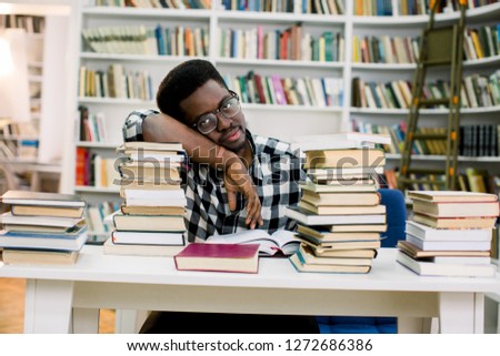 Ethnic african american guy lying at table surrounded by books in library. Student is bored and tired.