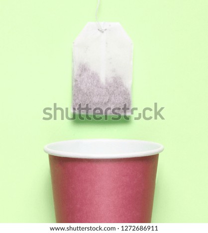 Empty disposable paper cup for tea, tea bag on green pastel background, top view, minimalism
