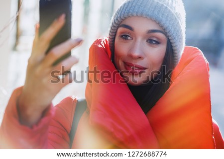 pretty woman make a smile portrait, and take a self portrait with her smart mobile phone. Girl takes fun winter selfie. Christmas, new year and winter holiday concept