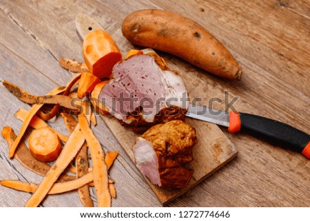 Raw sweet potato whole and chopped and homemade smoked meat on old cutting board