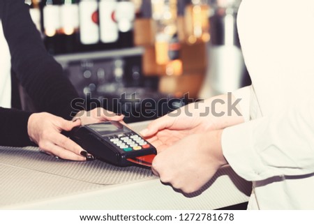 Credit card payment and electronic bank concept. Cashiers hand holds credit card terminal on defocused background. Payment for drink in bar. Customer puts credit card into machine