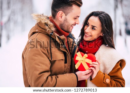 Celebration of St Valentine's day. Happy and beautiful young couple in love are walking together outdoors in winter city park and hugging and kissing each other. Gifts and flowers