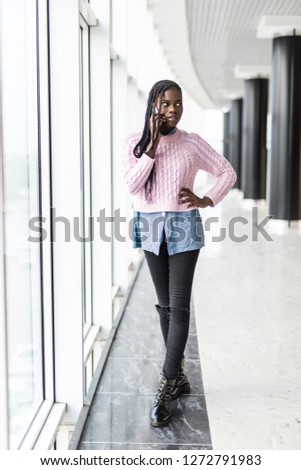 Full height of afro american woman talking mobile phone in front of panoramic window in comercial center