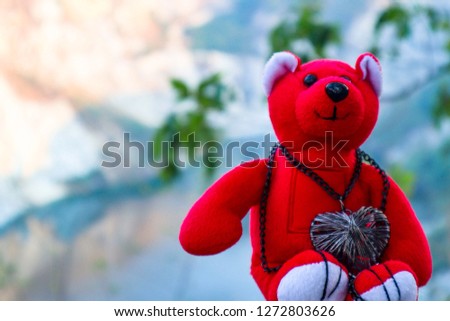 Red teddy bear wearing a heart-shaped necklace with space for text.