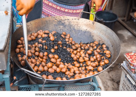 Hands grilling chestnuts in a wok in the market at the rural of Thailand