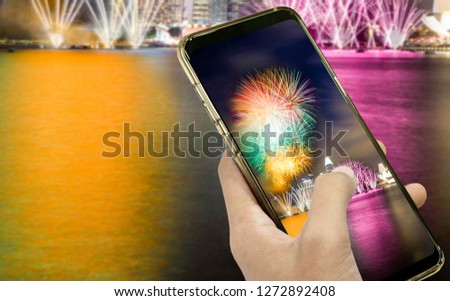 Hand of a businessman holding a smartphone to take a pictures at night and fireworks on dark sky for design idea in your work.