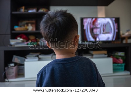 back view image of cute little kid watching flat screen LED television inside a house