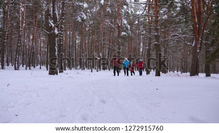 happy children and mom and dad run with the children in the winter forest. parents play with children in a snowy park in winter. happy family walks in Christmas forest. teamwork