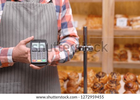 Cashier holding payment terminal in bakery, closeup. Space for text