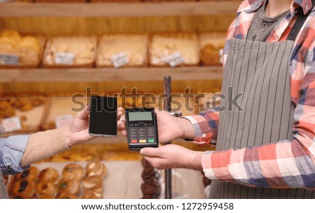 Woman using terminal for contactless payment with smartphone in bakery, closeup