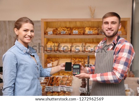 Woman using terminal for contactless payment with smartphone in bakery