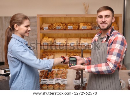 Woman using terminal for contactless payment with smartphone in bakery