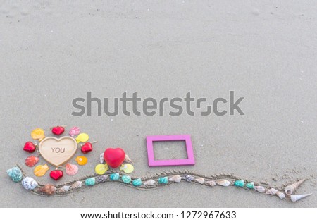   Valentine  concept  setting  with   colorful  seashells,brown  wooden  plate,red  hearts  and  pink  wood picture frame  on  sandy  beach  background