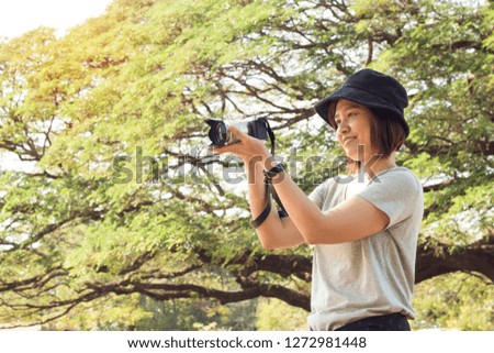 Asian women tourists Is taking pictures of nature with her camera on a clear day, the back is a big green tree with a beautiful shape
She smiles and is happy with this tour.