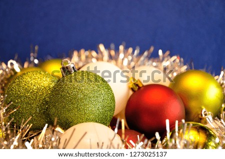 Different color Christmas baubles with silver tinsel against a blue background
