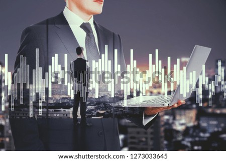 Young european businessman standing on abstract night city background with laptop. Trade and technology concept. Double exposure 