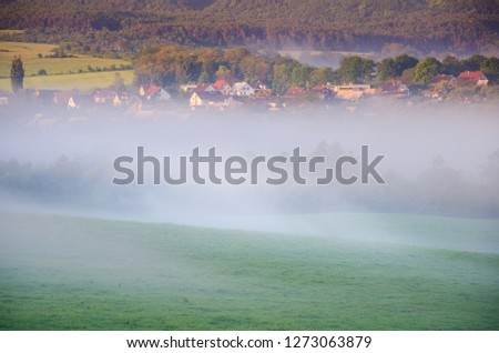 Landscape with rye field, hills, trees in morning mist and with beautiful colors of sunrise light. Wonderful wallpaper from summer morning.