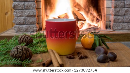 Merry Christmas near cozy fireplace, with mug of hot drink, cinnamon sticks, cones, nuts, tangarine over old brown desk ,in country house.