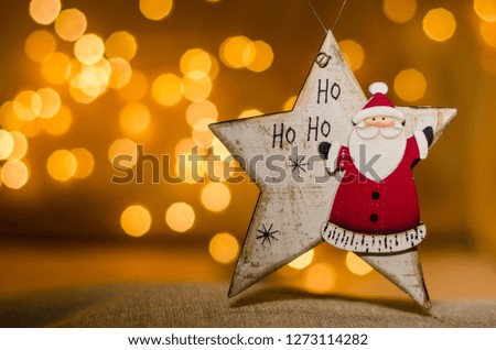 Christmas decorations for house interiors. Bokeh lights on the blurry background. Christmas and New Year toy. Wooden star with drawn Santa Clause and written ‘Ho Ho Ho’.