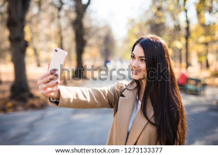 Beautiful young woman taking a selfie with smartphone in park in autumn.