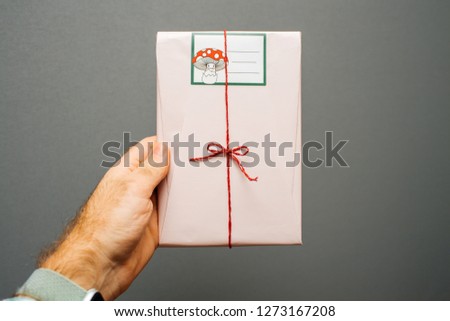 Man hand holding against gray background gift wrapped in pink festive paper - delicate design handmade packaging