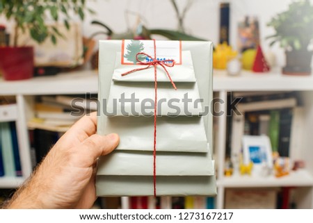 Man hand holding against bookcase background gift wrapped in festive paper with fir tree silhouette - delicate design handmade packaging