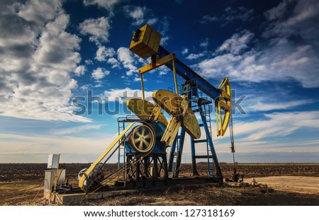 Operating oil well profiled on dramatic cloudy sky Royalty-Free Stock Photo #127318169